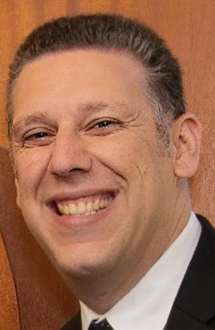 a man wearing a suit and tie smiling and looking at the camera