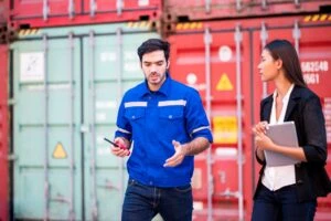 Two people standing in front of shipping containers.