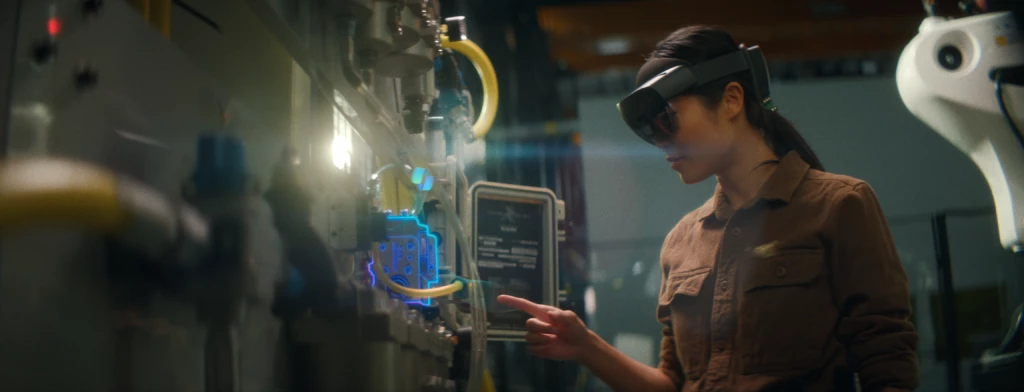 Woman in a HoloLens 2 gestures with her index finger at a machine. The part she points to is lit up with a holographic outline.