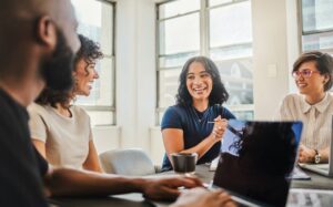 A diverse group of coworkers collaborate in an office space while one takes notes on his laptop.