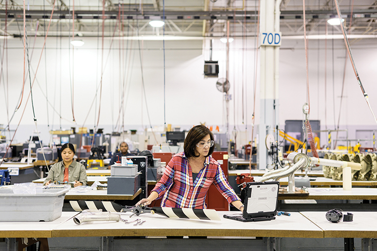 製造ラインで PC をチェックしながら部品を組み立てる女性