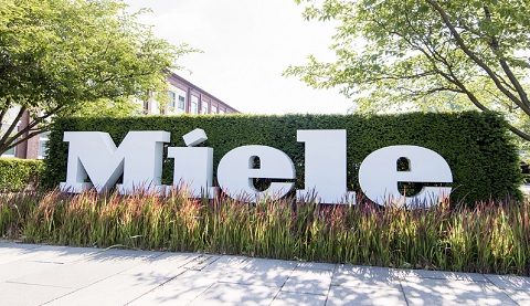 Das Miele Logo ist vor einer Hecke zu sehen.