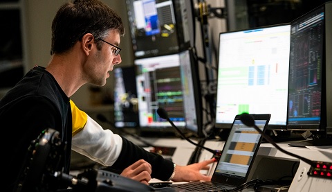 Ein Mann arbeitet an einem Schreibtisch, vor ihm mehrere Bildschirme. 