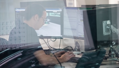 Ein Mann, der an seinem Schreibtisch arbeitet, spiegelt sich in einer Glasscheibe 