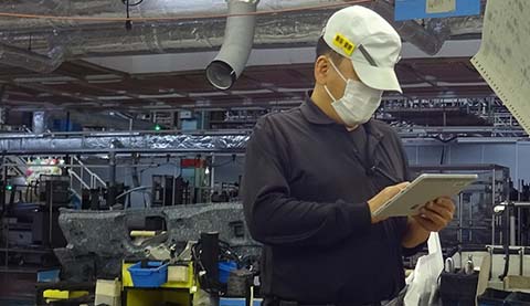 A man is standing in a factory while he is holding a table PC