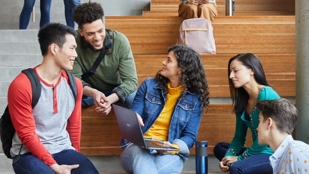 F&uuml;nf Student*innen sitzen in einer Aula und unterhalten sich.