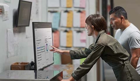 Zwei Menschen vor einem großen Tisch Bildschirm wobei eine Frau etwas erklärt.