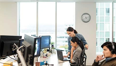 Drei Personen in einem Büro, im Hintergrund große Fenster.