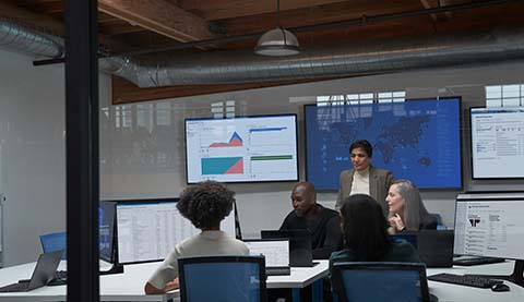 Büroraum mit fünf Personen und sehr vielen Bildschirmen.