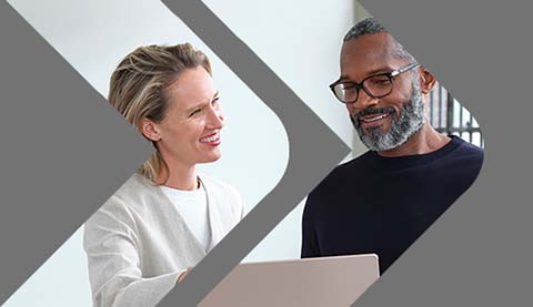 Mann und Frau blicken auf einen Laptop und lächeln dabei.