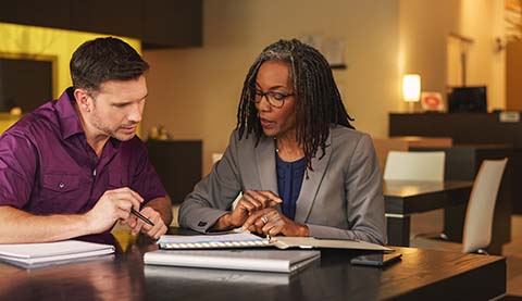 Eine Finanzberaterin und ein Kunde an einem Schreibtisch während sie auf einen Block Papier blicken.