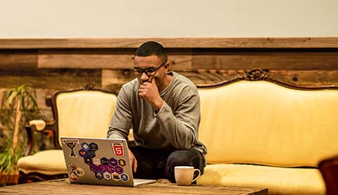 Mann auf einer beigen Couch an einem niedrigen rustikalen Tisch.