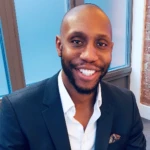 Zephaniah Chukwudum, a man wearing a suit and tie smiling at the camera