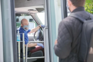 Intelligent automation can help deliver vital services. A man gets on a bus. The bus driver is wearing PPE.