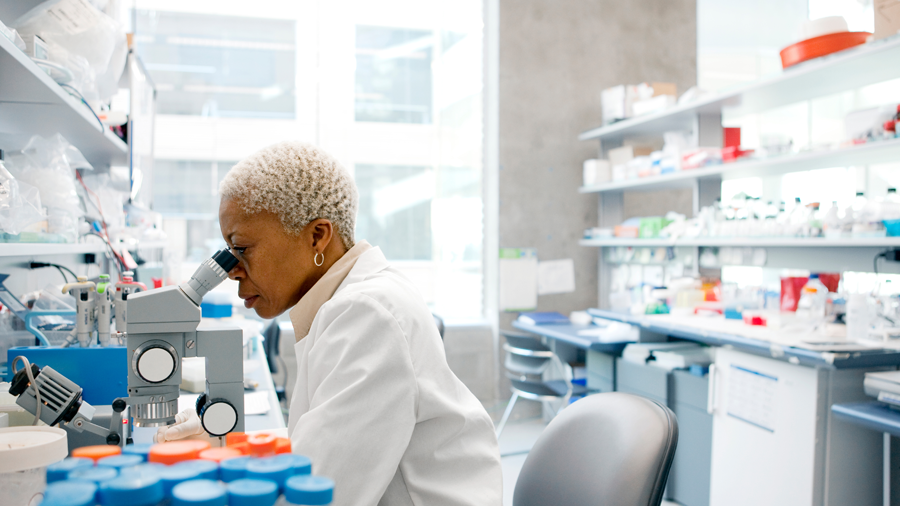 Scientist in lab coat looking through microscope.