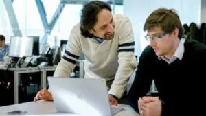 Two men over a laptop on a desk