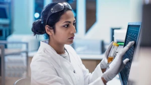 Woman in lab goggles and gloves working on a monitor
