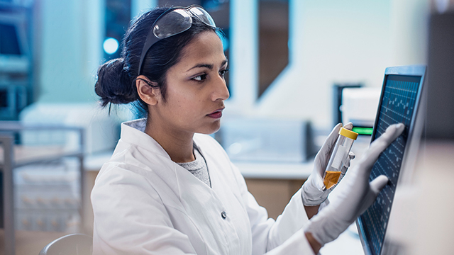 Woman in lab goggles and gloves working on a monitor