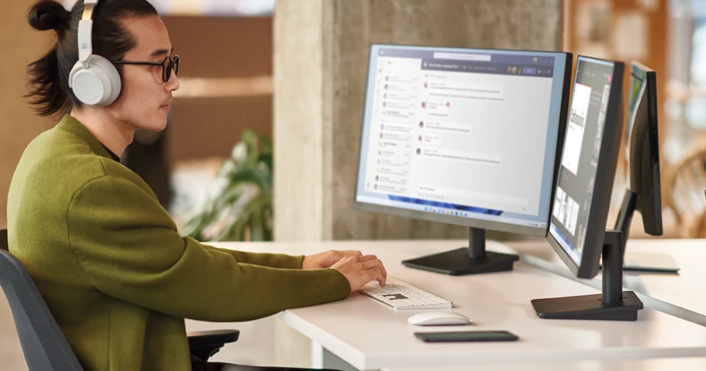 Employee collaborating during a Microsoft Teams meeting while working in an open office setting on dual monitor.