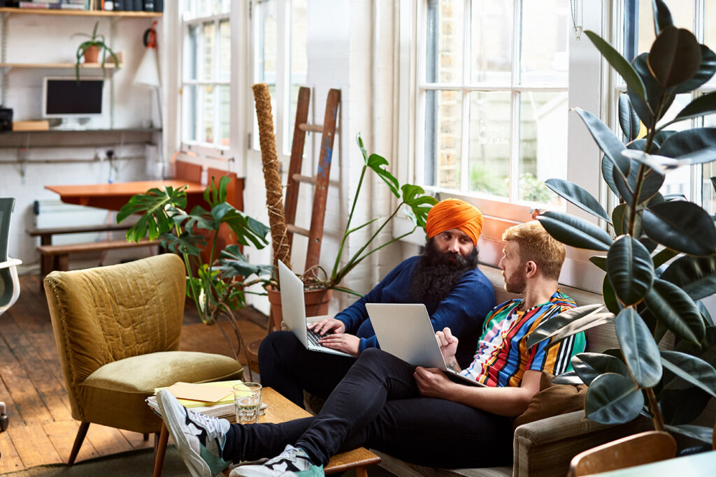 A couple of men sitting on a couch with laptops