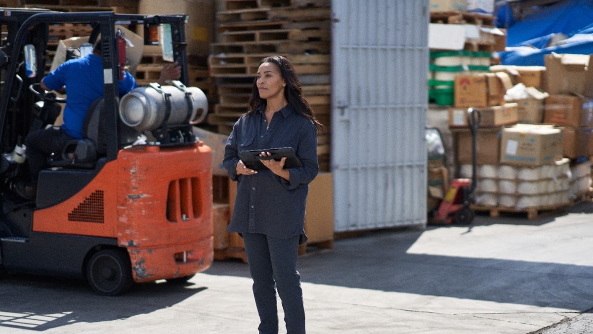 Female manufacturing worker holding tablet device while monitoring work outside of a factory.