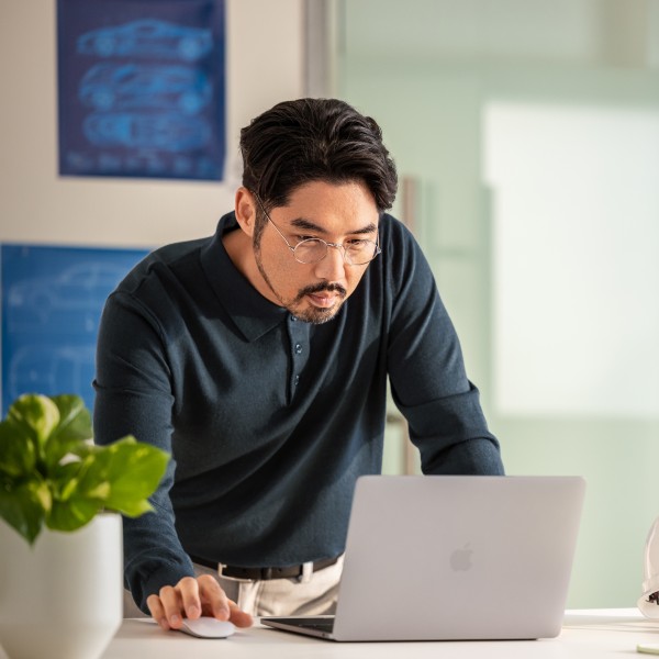 A man in glasses, standing, looking at a laptop on a counter.