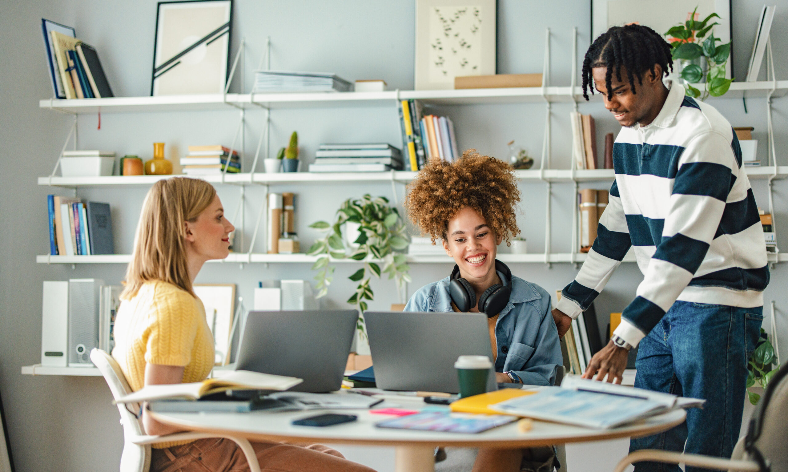 Three students working on laptops at a round table.