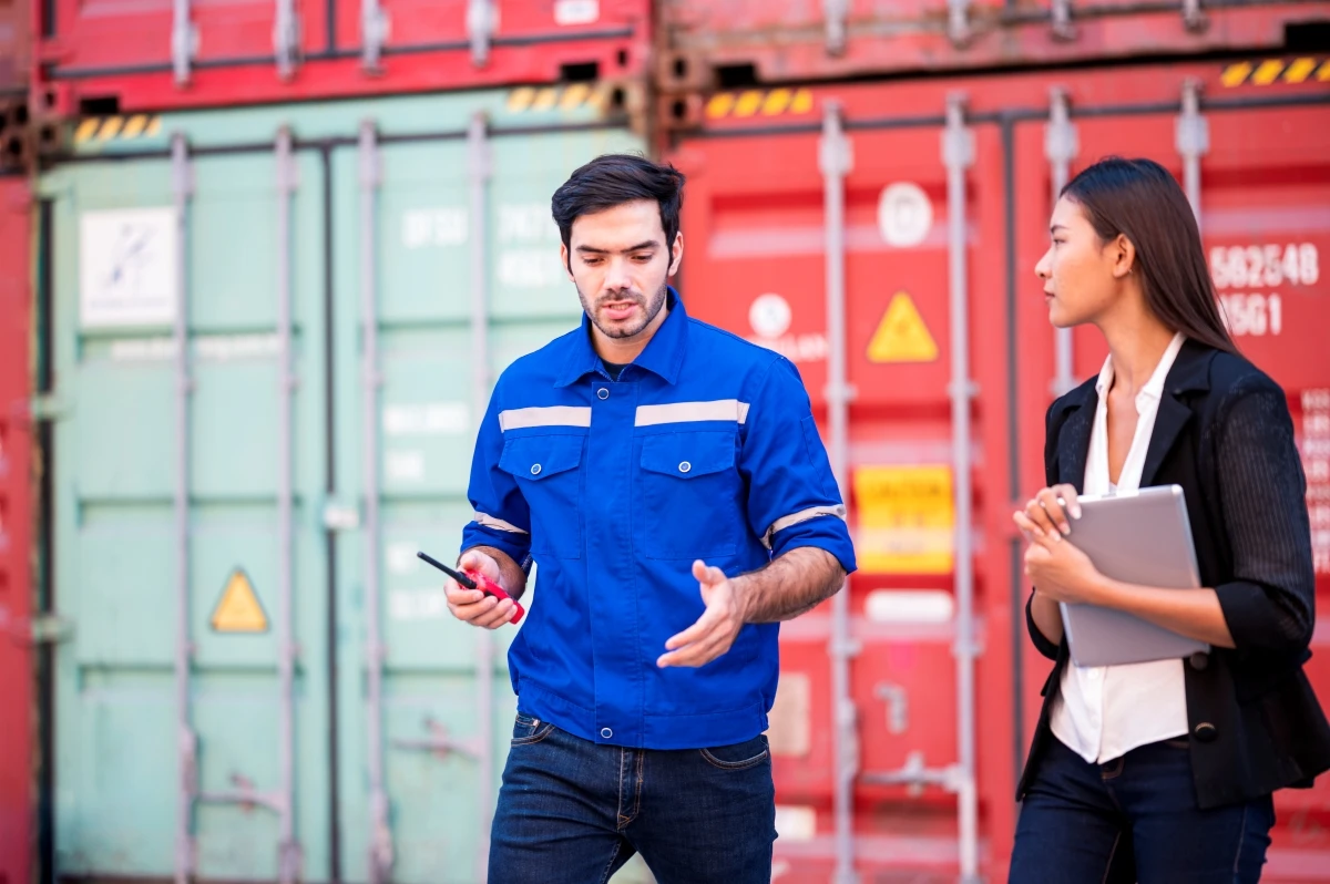 Two people standing in front of shipping containers.