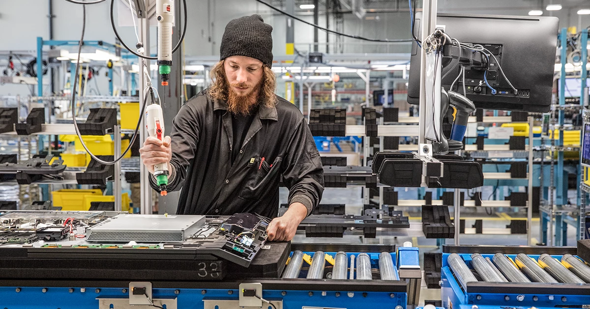 Male millennial factory worker building computer parts on assembly line