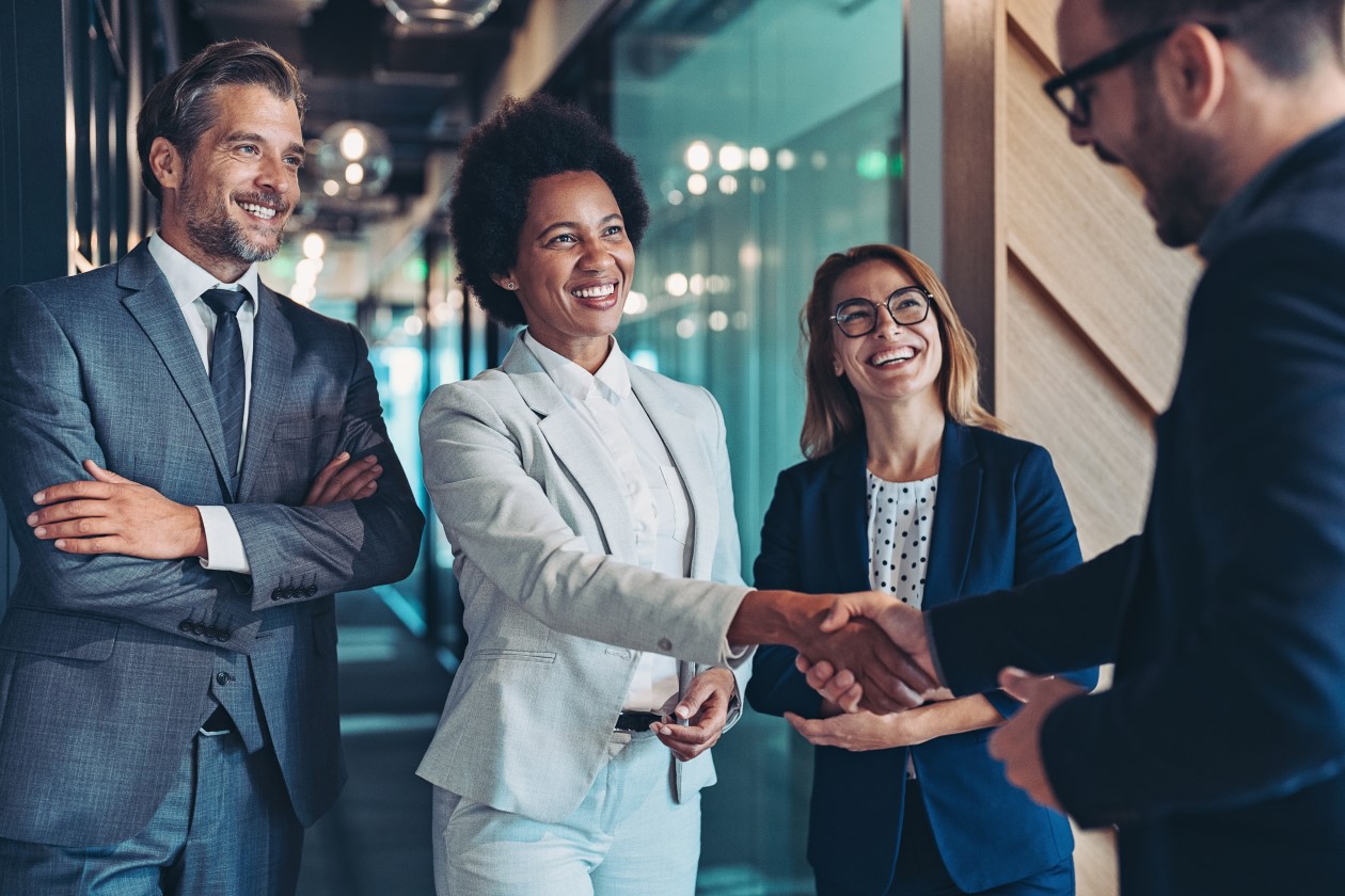 Four business people smiling, two of which shaking hands.