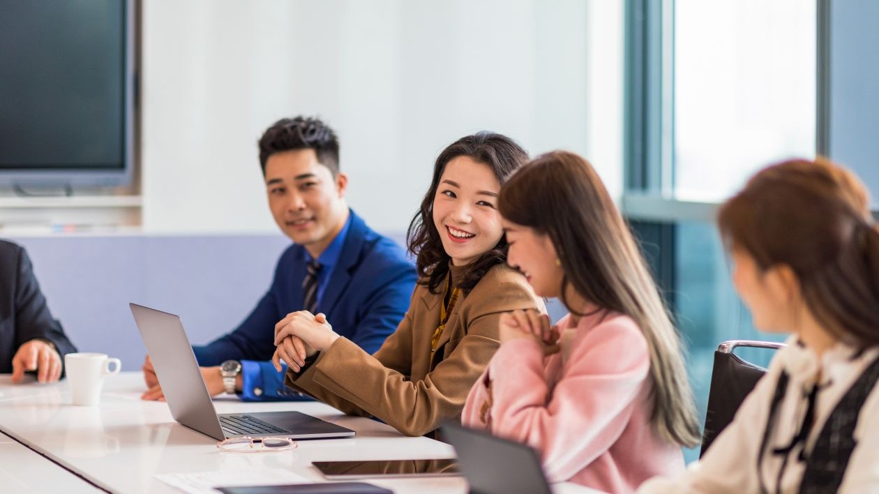 A group of smiling businesspeople collaborate in a meeting room.