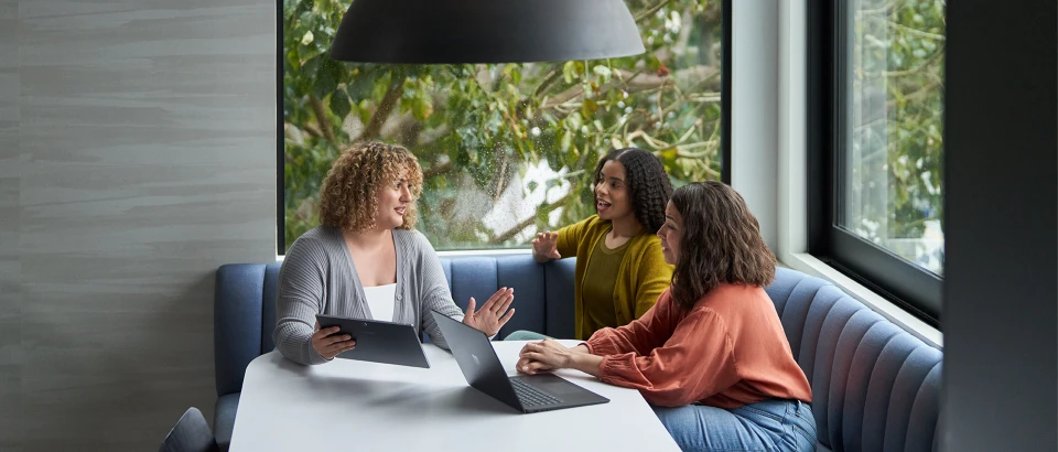 Three people dressed in casual sweaters engaged in discussion with 2 laptops open on a table in front of them