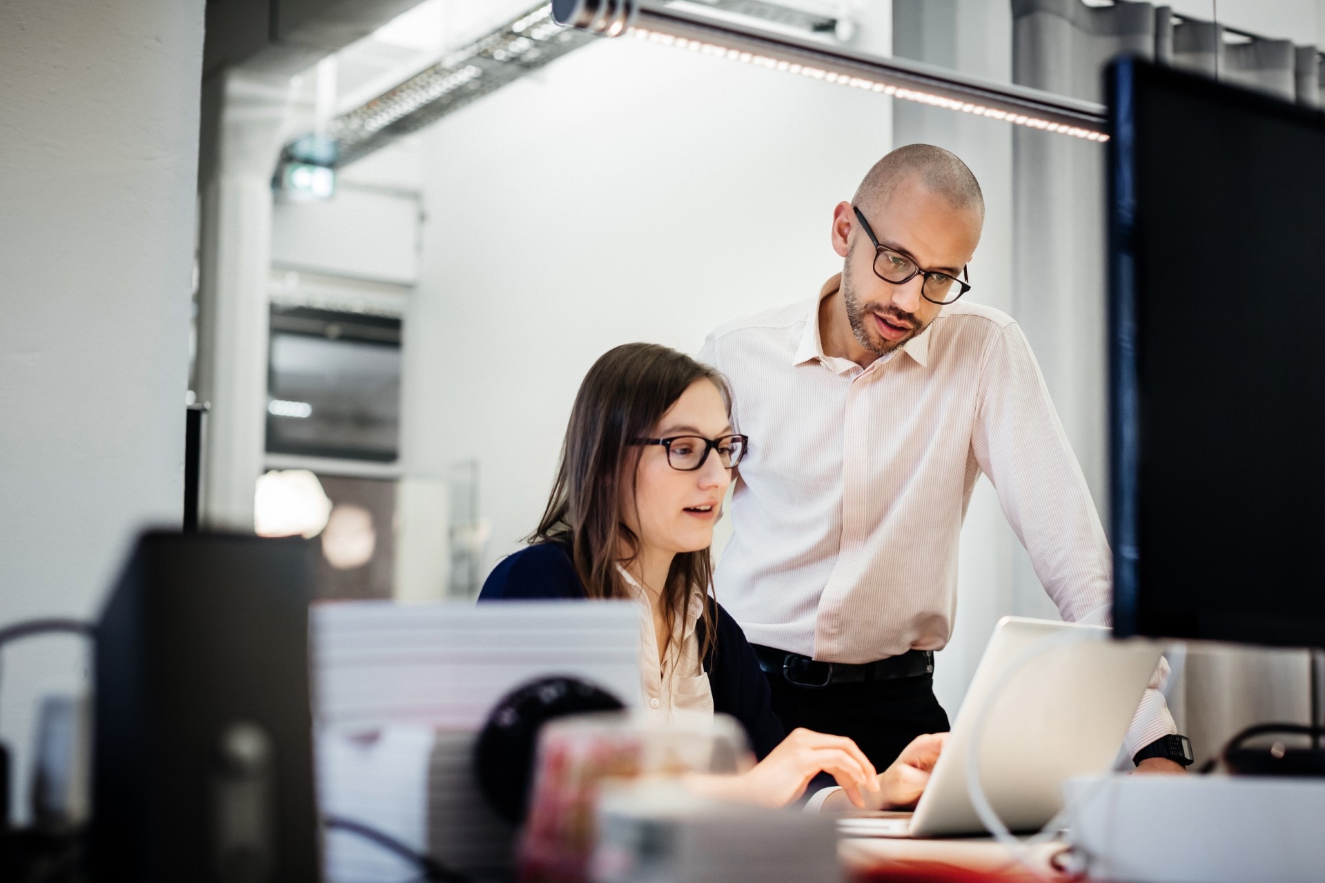 Two professionals collaborating at a desk, reviewing information on a laptop screen in a modern office setting.