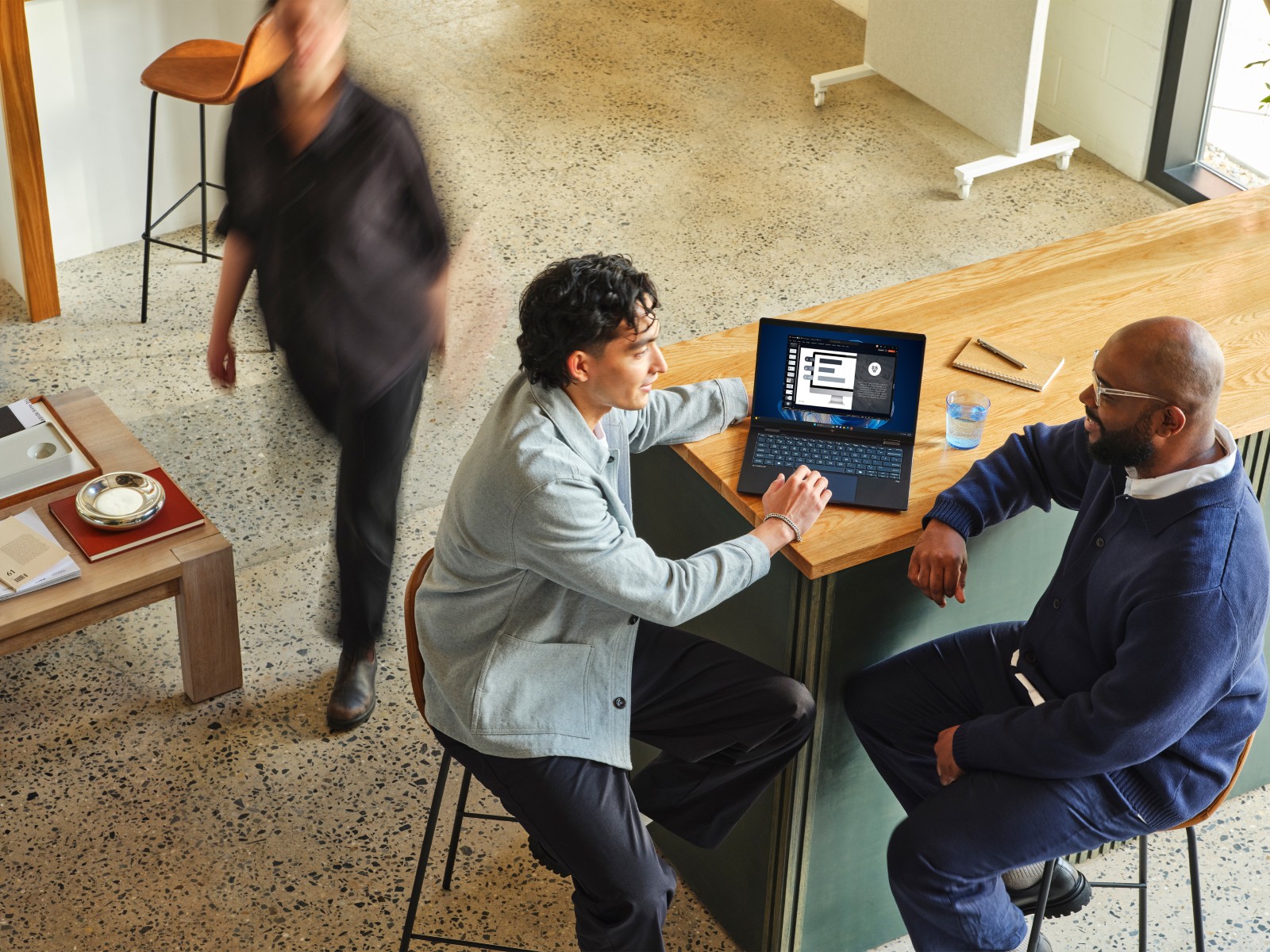 Two people in conversation while reviewing information on a laptop in a professional setting.
