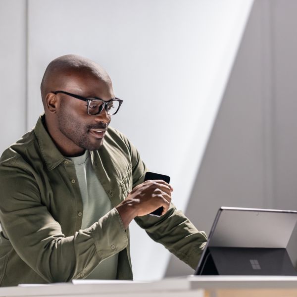 A person in focused work using a Surface tablet while holding a mobile device.