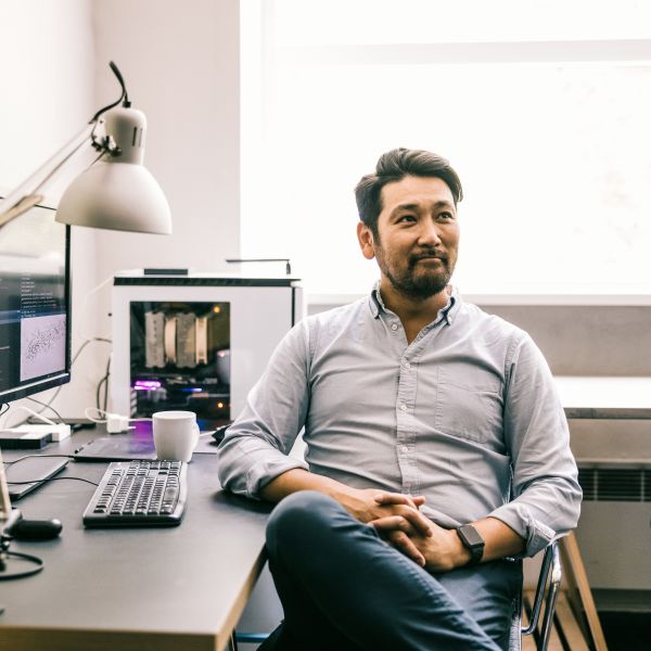 A person at a desk looks off‑screen from their computer with a confident, accomplished expression.