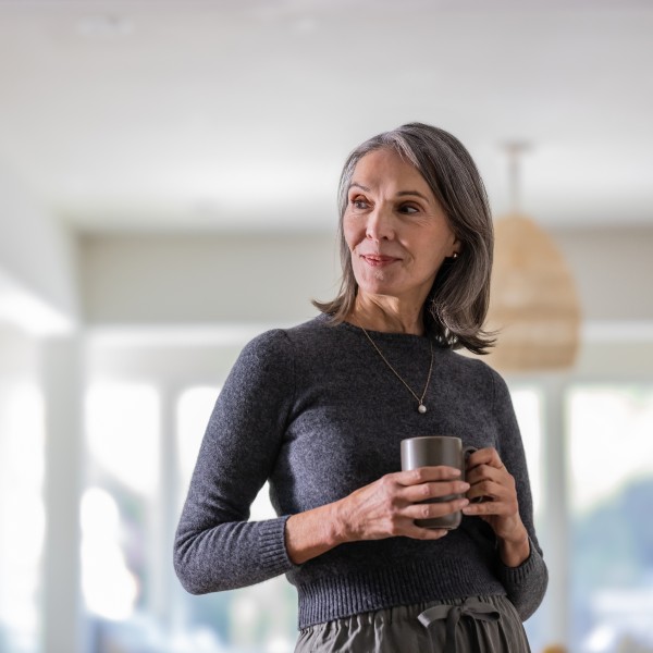 A woman, standing holding a mug, looking off to her right