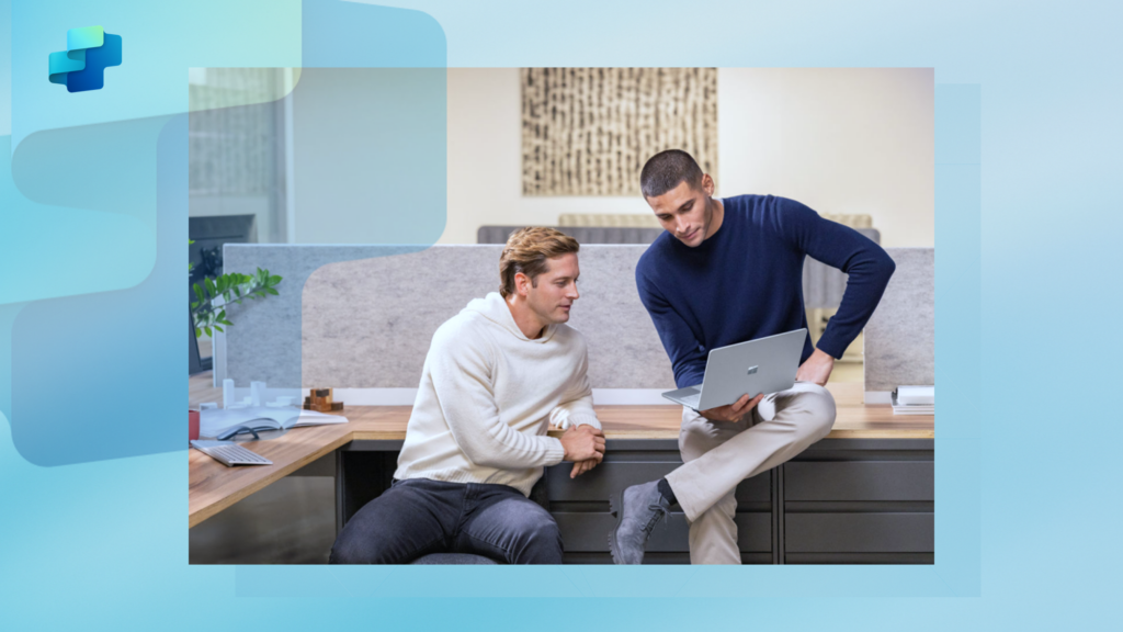 A man sitting on a desk showing another person a laptop screen