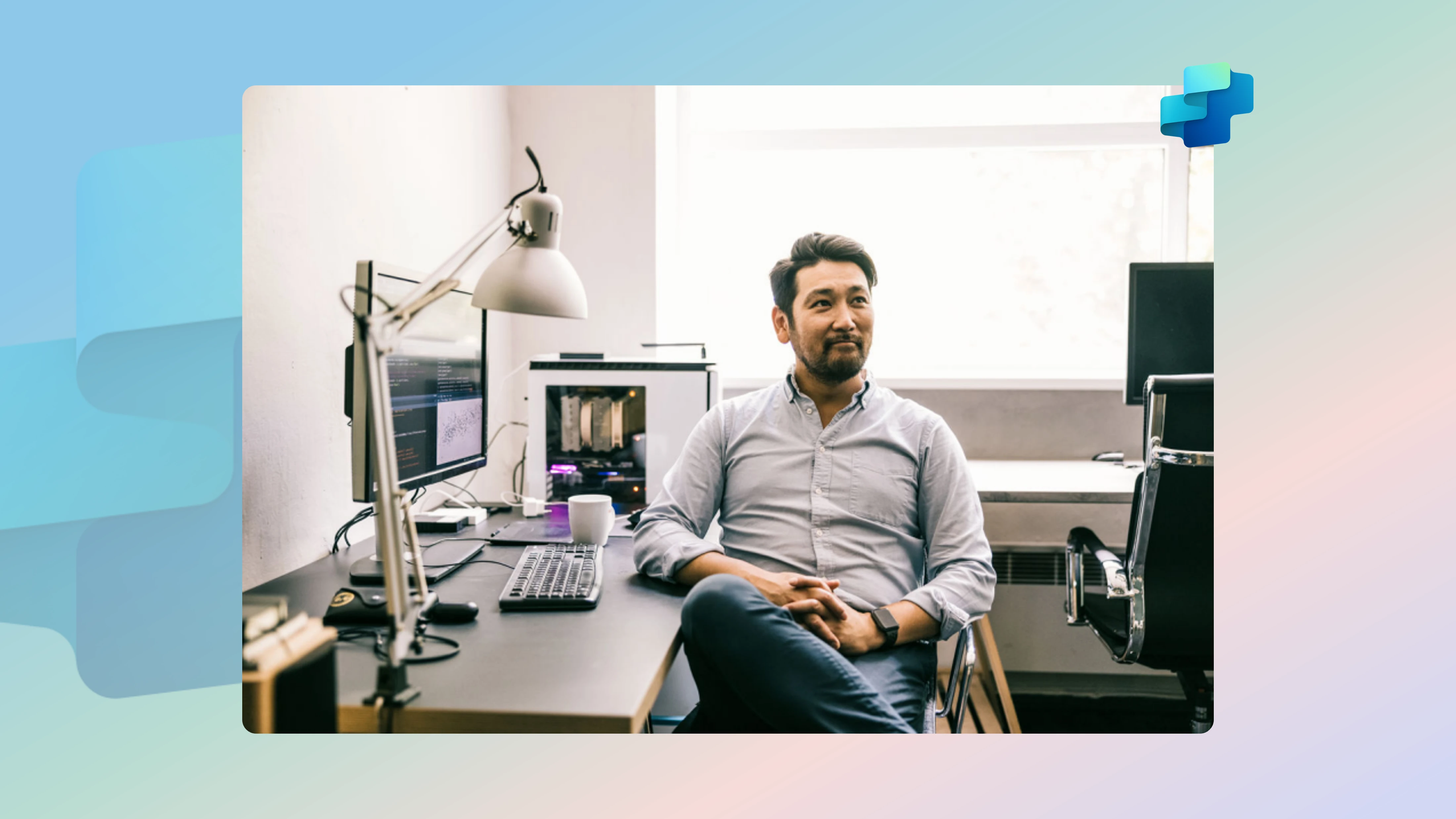 A man sitting at a desk with his legs crossed, looking contentedly away from his screen