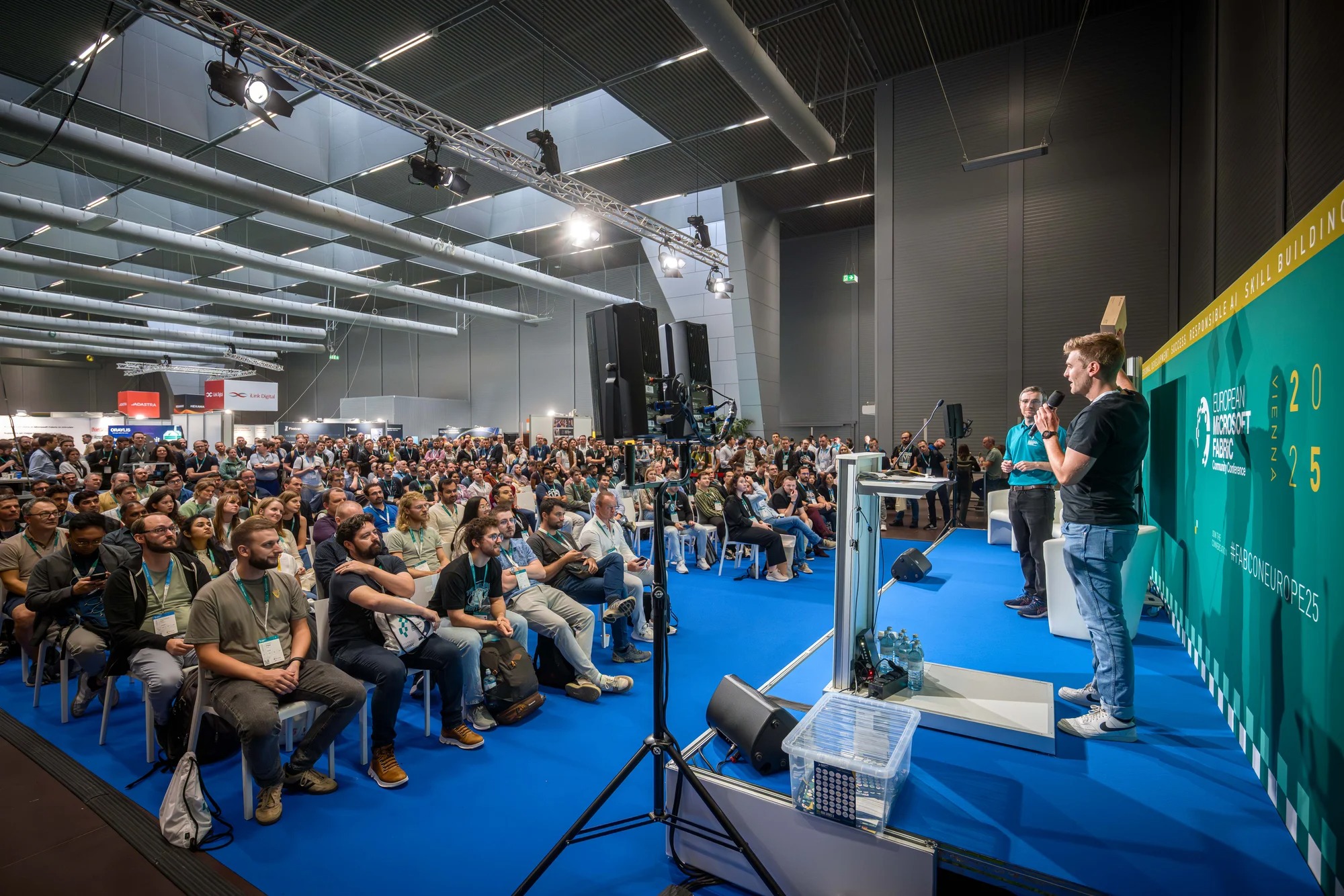 A speaker stands on a stage in front of a crowd at the 2025 Fabric Community Conference.