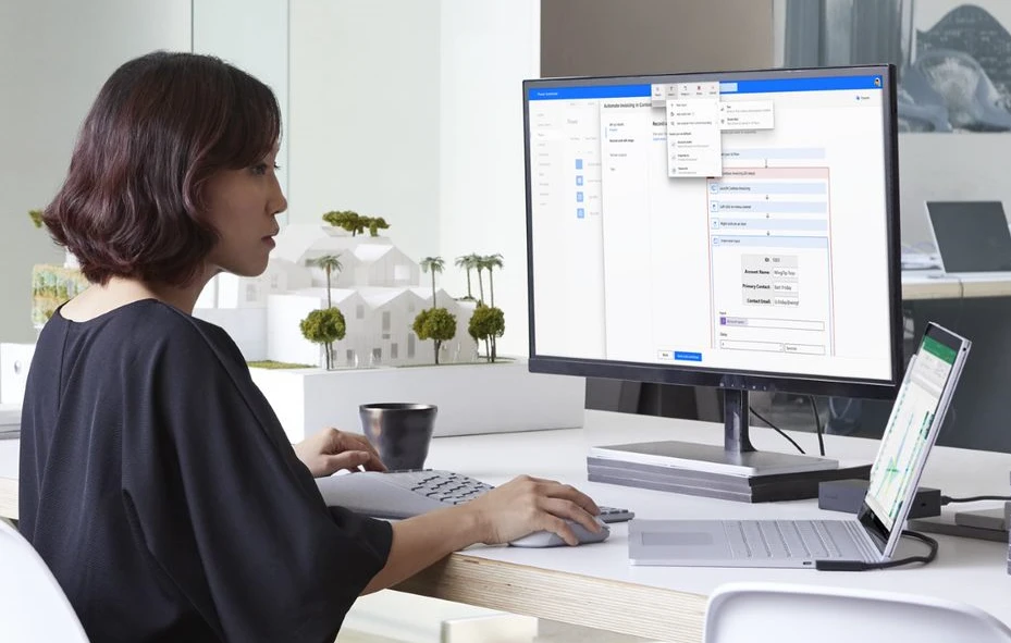 Woman sits at desk using laptop and second monitor.