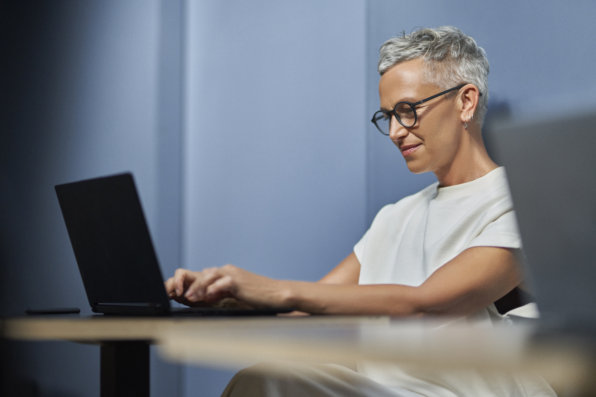 Woman smiling in workspace while on laptop.