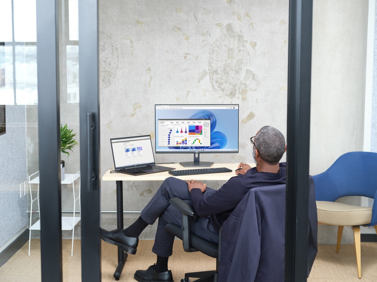 Man sitting in an office viewing Power BI UI within Windows 365. Shown on Windows 11. Keywords: sitting at a desk; crossed legs; Markus Long; Fabrikam; Enterprise; mousing; laptop; desktop; one screen; one monitor; dual screens; Edge browser; backside of person; Swanson