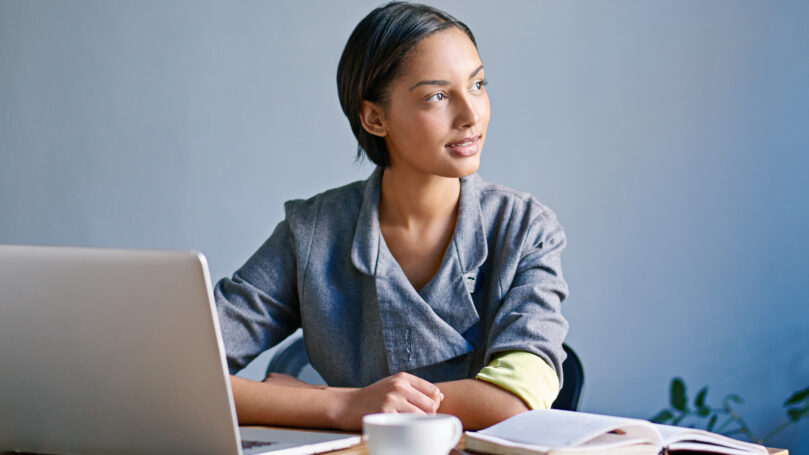 A woman sitting at a desk with a laptop and a cup of coffee