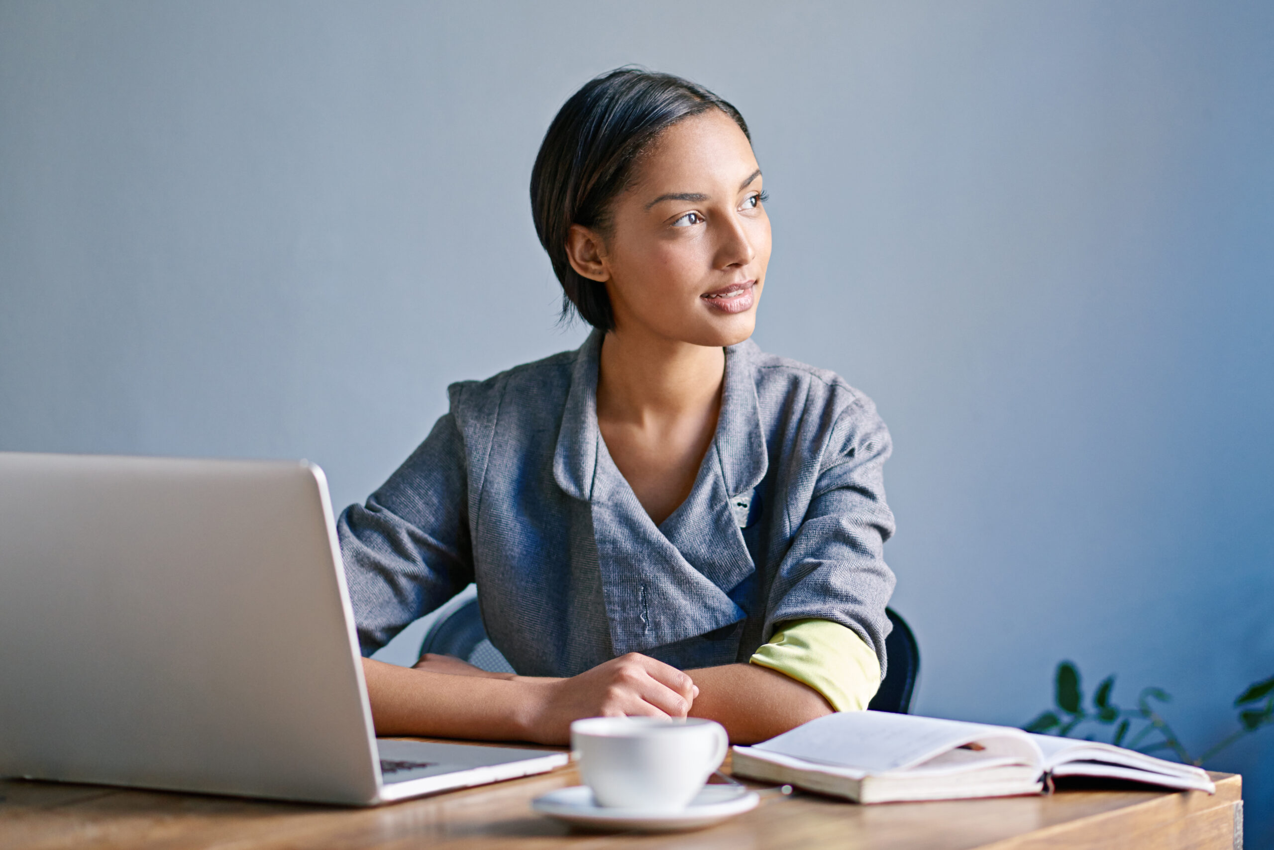 A woman sitting at a desk with a laptop and a cup of coffee