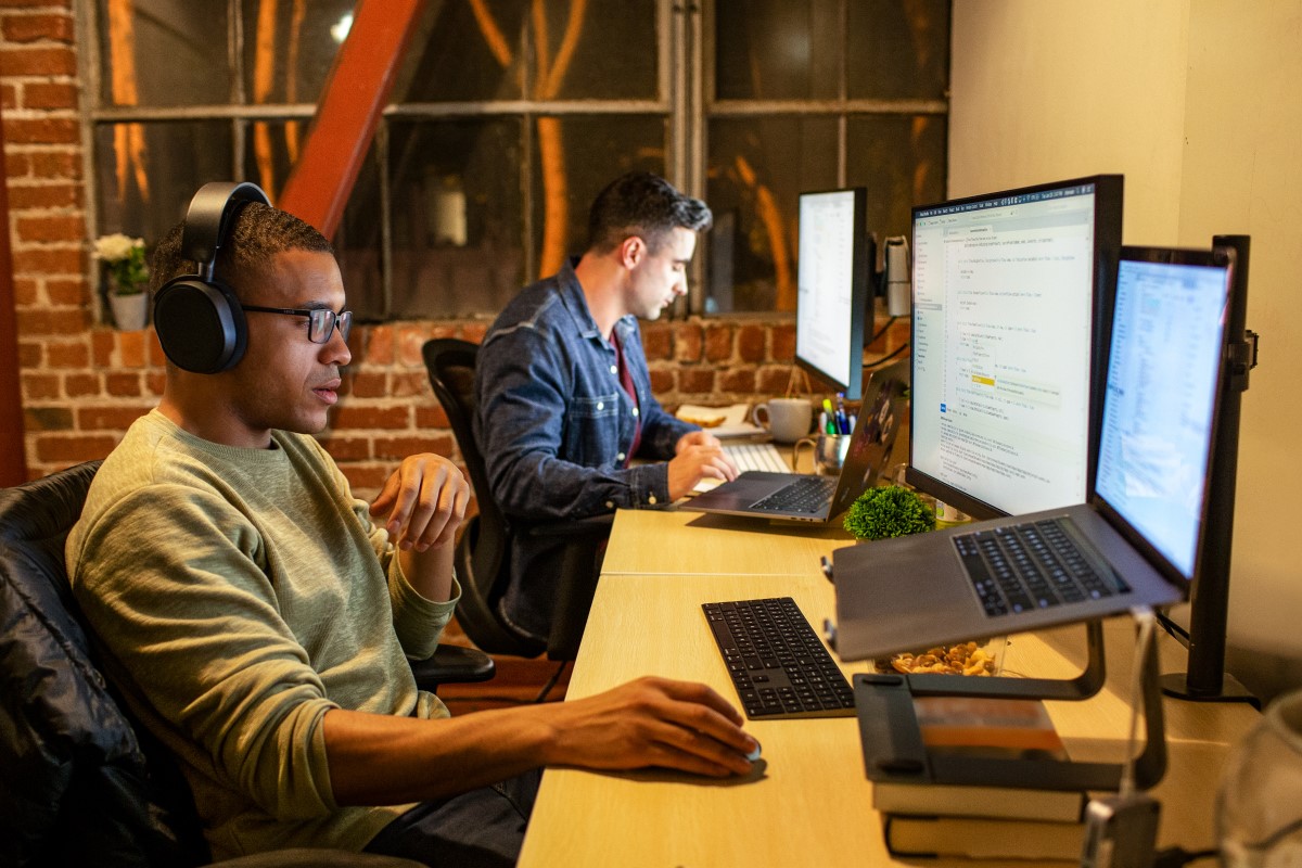 Two male developers in focused work in n casual enterprise office. One is wearing headphones.