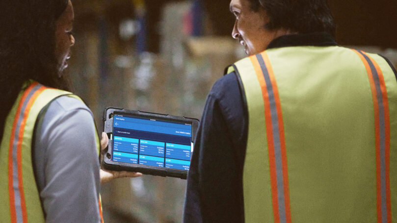 A man and woman in safety vests looking at a tablet