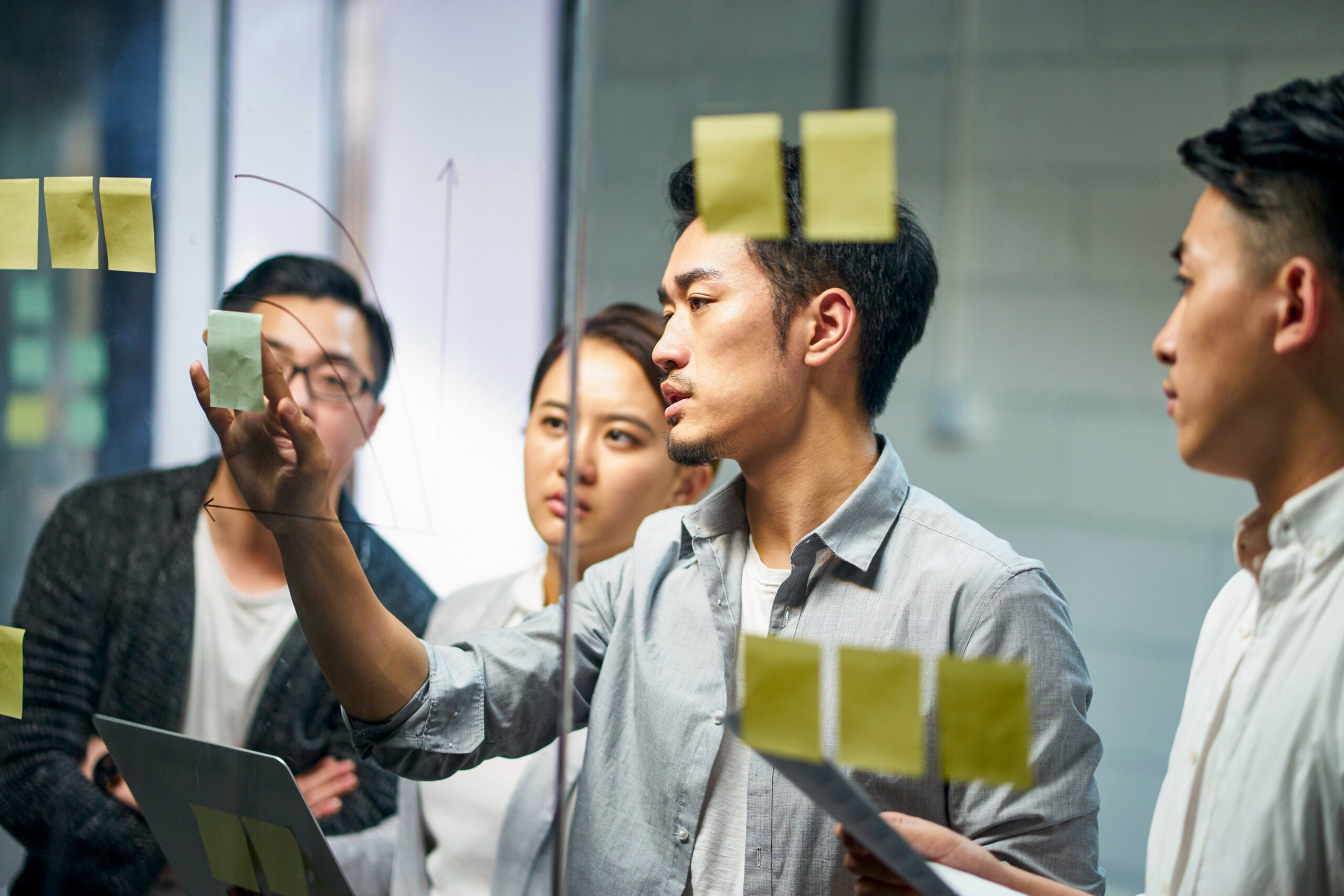 A group of people looking at sticky notes on a glass wall