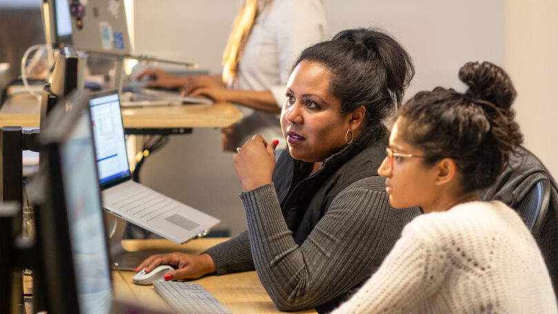 Two developers working at desk with monitors.