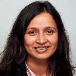 Professional headshot of a person wearing a dark blazer and striped button-down shirt against a neutral background.